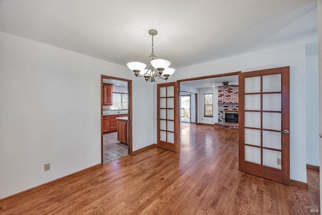 unfurnished dining area with light wood-style flooring, french doors, baseboards, a brick fireplace, and a chandelier