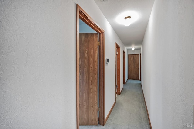 corridor with baseboards and light colored carpet