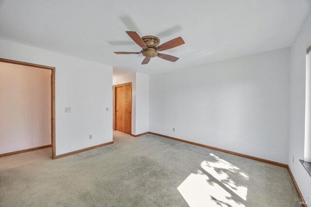 spare room featuring a ceiling fan, light colored carpet, and baseboards