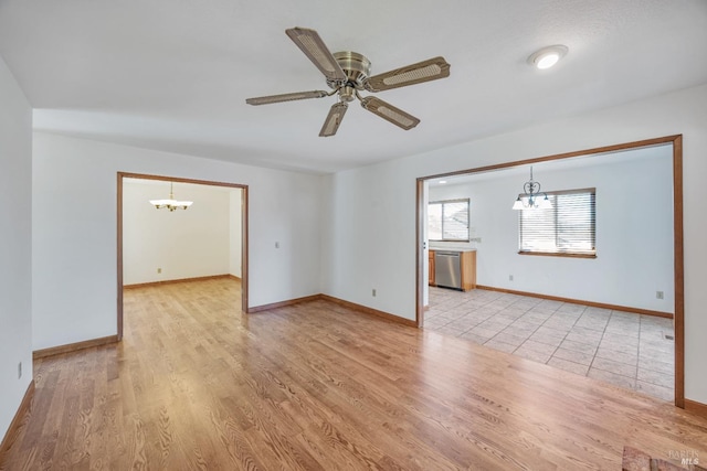 spare room featuring ceiling fan with notable chandelier, baseboards, and light wood-style floors