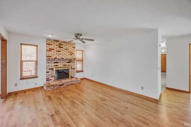 unfurnished living room with light wood-style flooring, a brick fireplace, baseboards, and ceiling fan