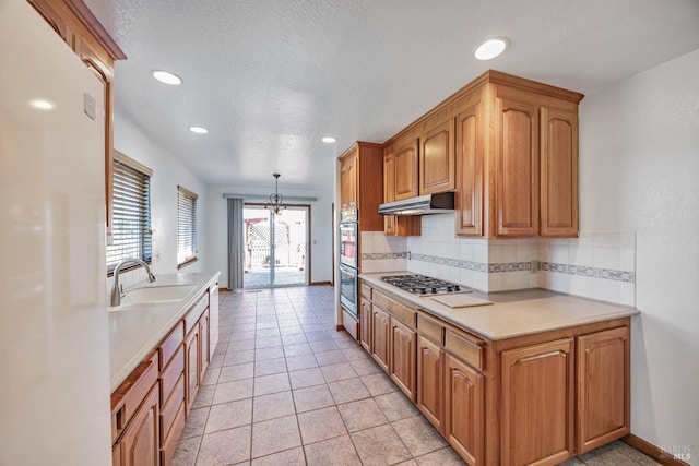 kitchen with under cabinet range hood, a sink, backsplash, appliances with stainless steel finishes, and light countertops