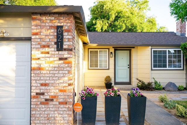 entrance to property featuring a garage, brick siding, a chimney, and a shingled roof