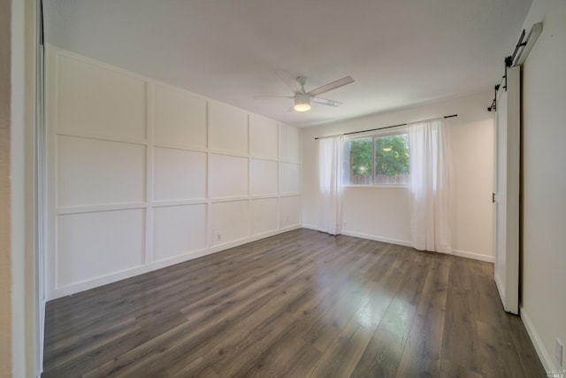 unfurnished room with ceiling fan, baseboards, a barn door, and dark wood-type flooring