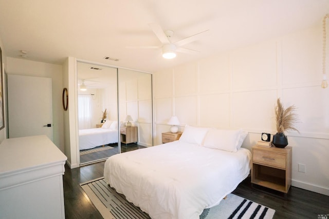 bedroom featuring dark wood-style floors, visible vents, a ceiling fan, a closet, and a decorative wall