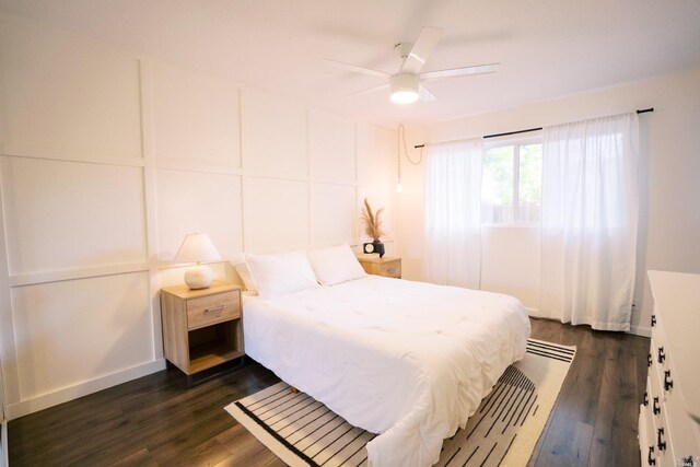 bedroom featuring ceiling fan, baseboards, dark wood-style floors, and a decorative wall