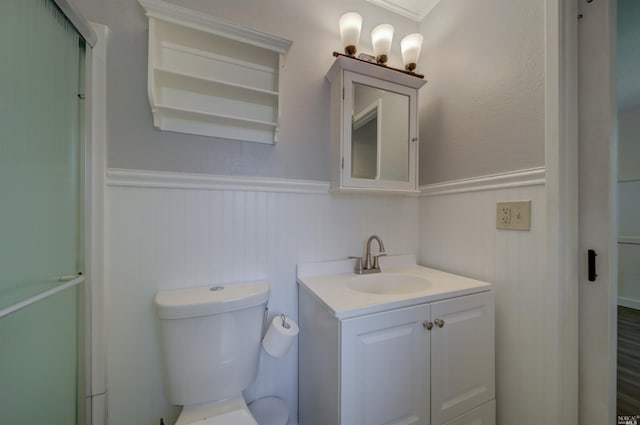 bathroom with a wainscoted wall, vanity, a shower with door, and toilet