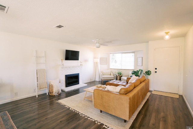 living room with a ceiling fan, visible vents, dark wood-style floors, and a brick fireplace