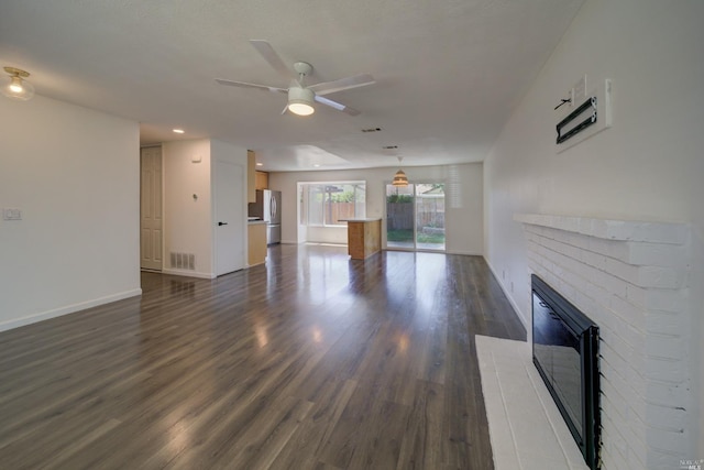 unfurnished living room featuring visible vents, dark wood-type flooring, a ceiling fan, baseboards, and a brick fireplace