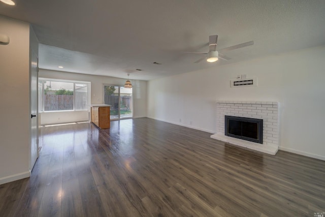 unfurnished living room with ceiling fan, a brick fireplace, baseboards, and dark wood-style flooring