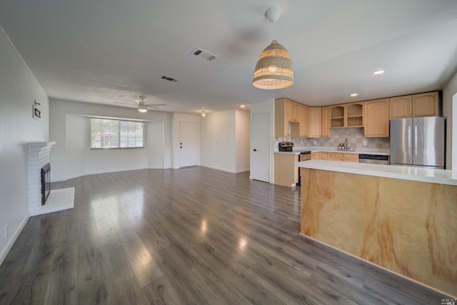 kitchen featuring light brown cabinetry, backsplash, stainless steel appliances, a fireplace, and light countertops