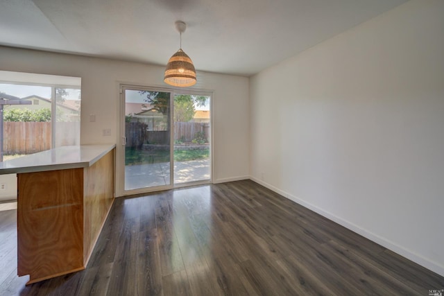 unfurnished dining area featuring baseboards, plenty of natural light, and dark wood-style flooring