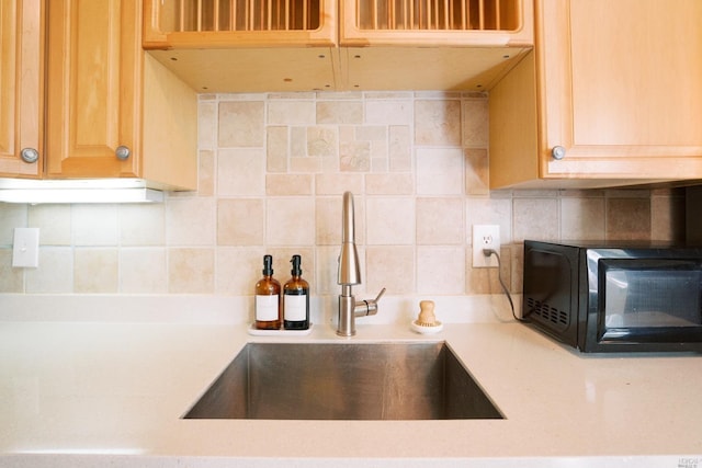 kitchen with black microwave, light countertops, a sink, and backsplash