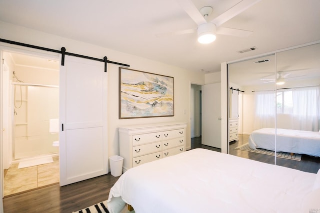 bedroom with a barn door, dark wood finished floors, visible vents, ensuite bath, and ceiling fan
