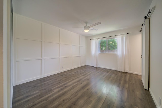 empty room with a barn door, a ceiling fan, and dark wood-style flooring