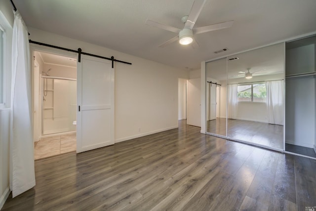 unfurnished bedroom with visible vents, wood finished floors, a barn door, connected bathroom, and ceiling fan