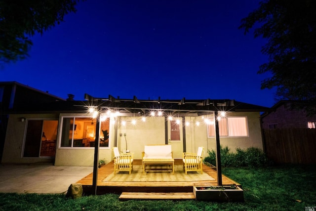 back of house at night featuring fence, an outdoor hangout area, stucco siding, a wooden deck, and a patio area