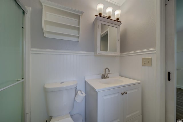 bathroom with vanity, toilet, a wainscoted wall, and a shower with door