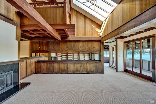 kitchen featuring beam ceiling, high vaulted ceiling, carpet floors, a skylight, and wood walls