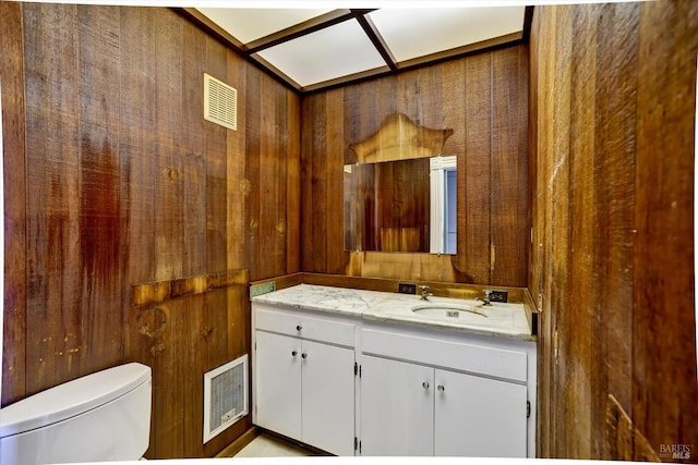 half bathroom with visible vents, toilet, vanity, and wooden walls