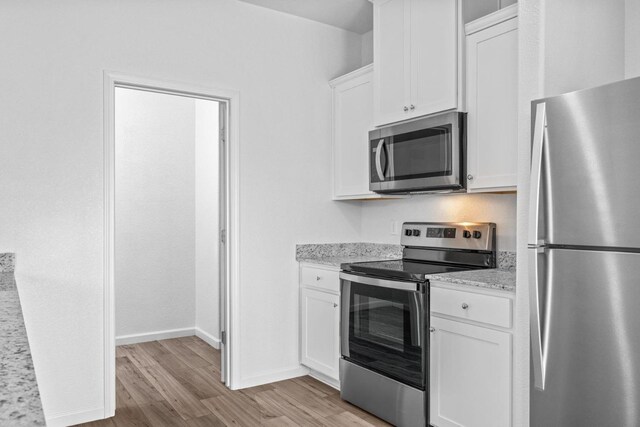 kitchen featuring light stone counters, light wood-style floors, appliances with stainless steel finishes, white cabinets, and baseboards