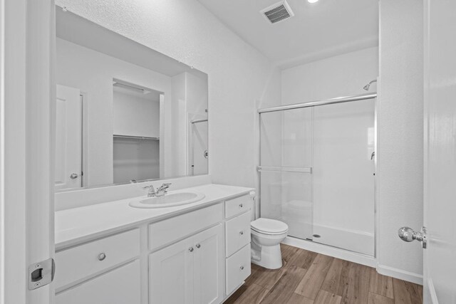 bathroom featuring a shower stall, toilet, wood finished floors, and visible vents