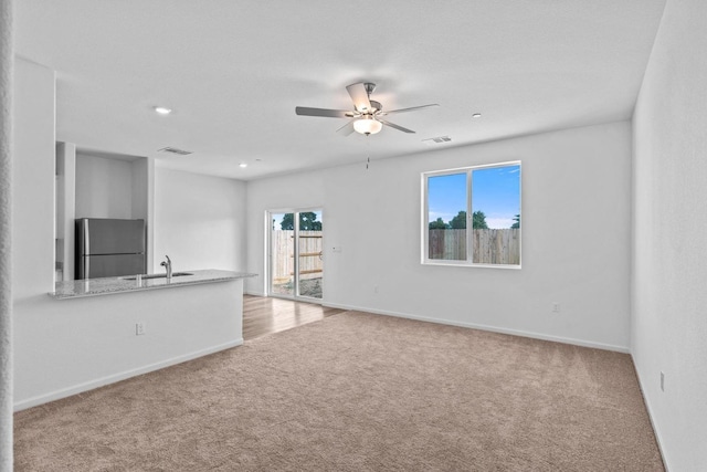 unfurnished living room featuring a sink, visible vents, ceiling fan, and carpet flooring