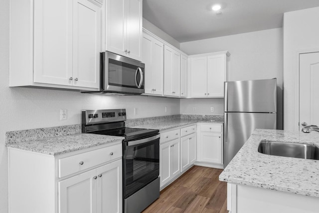 kitchen with wood finished floors, appliances with stainless steel finishes, white cabinetry, a sink, and light stone counters