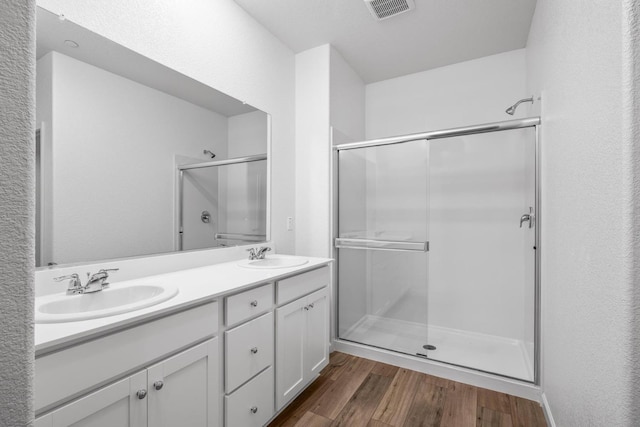 bathroom with a sink, visible vents, wood finished floors, and a shower stall