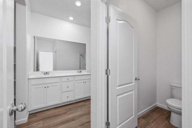 bathroom featuring toilet, a sink, wood finished floors, double vanity, and baseboards