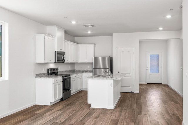 kitchen featuring wood finished floors, light stone countertops, an island with sink, stainless steel appliances, and white cabinetry