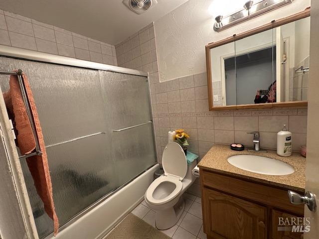 full bath with tile patterned flooring, visible vents, vanity, combined bath / shower with glass door, and tile walls