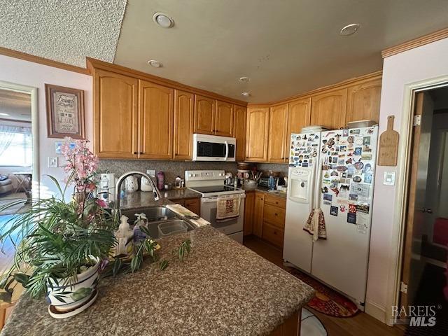 kitchen with a sink, decorative backsplash, white appliances, and ornamental molding