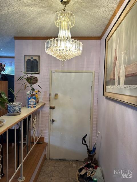 entryway featuring a textured ceiling, a chandelier, and ornamental molding