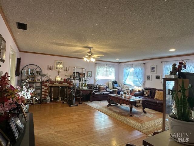 living room featuring visible vents, a textured ceiling, light wood-type flooring, and ornamental molding