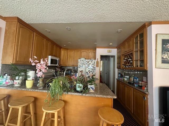 kitchen featuring stainless steel microwave, glass insert cabinets, a breakfast bar area, fridge with ice dispenser, and a peninsula