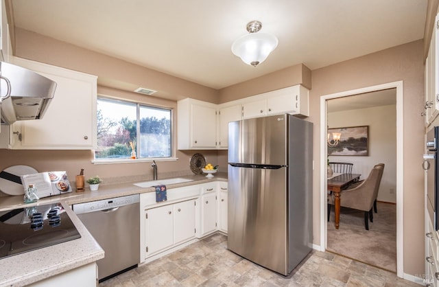 kitchen with a sink, stainless steel appliances, white cabinetry, and stone finish flooring