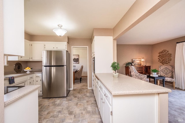 kitchen featuring stone finish flooring, light stone countertops, a peninsula, stainless steel appliances, and white cabinetry