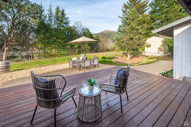 wooden deck with an outbuilding, outdoor dining space, fence, a mountain view, and a storage shed