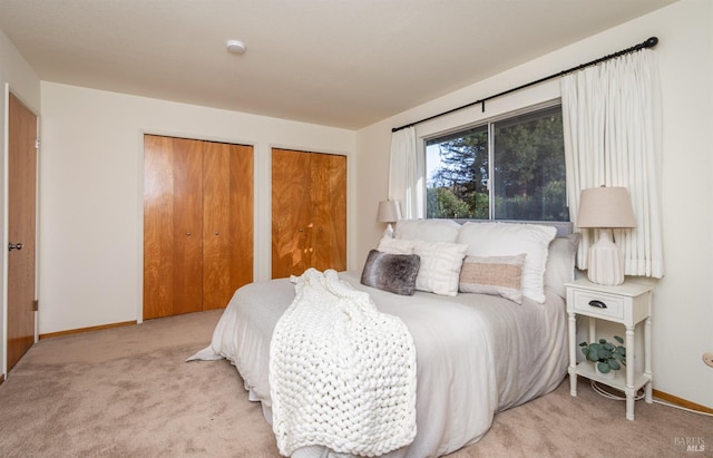 bedroom featuring multiple closets, light colored carpet, and baseboards