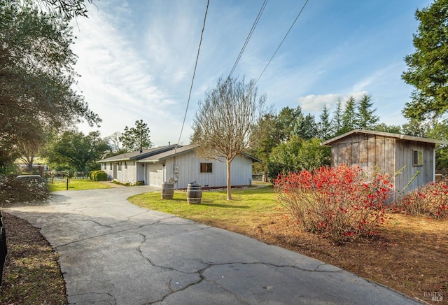 view of front of property featuring a front lawn, an attached garage, an outbuilding, and driveway