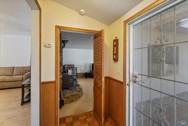 hallway featuring a textured ceiling, vaulted ceiling, wooden walls, and wainscoting