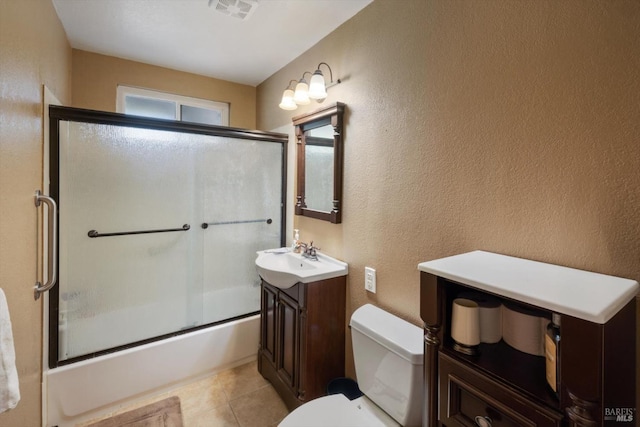 full bathroom featuring vanity, visible vents, bath / shower combo with glass door, toilet, and a textured wall