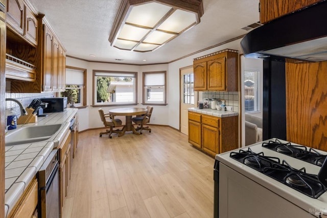 kitchen featuring tile counters, under cabinet range hood, ornamental molding, white range with gas cooktop, and light wood-style floors
