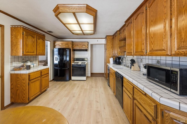 kitchen featuring brown cabinetry, light wood finished floors, a sink, black appliances, and tile counters