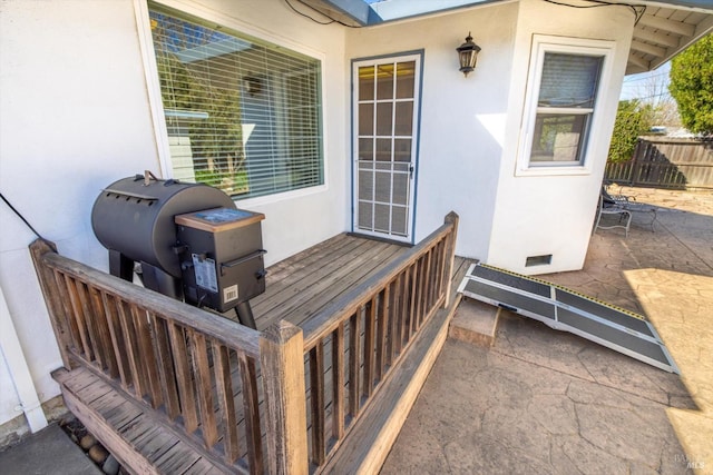 view of exterior entry with crawl space, a patio area, stucco siding, and fence
