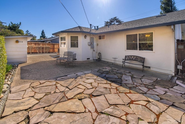 rear view of house featuring stucco siding, a shingled roof, a patio, and fence