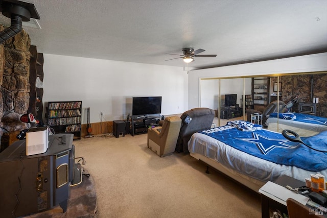carpeted bedroom with a ceiling fan, a textured ceiling, and a wood stove