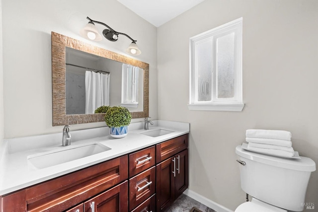 bathroom featuring double vanity, toilet, baseboards, and a sink