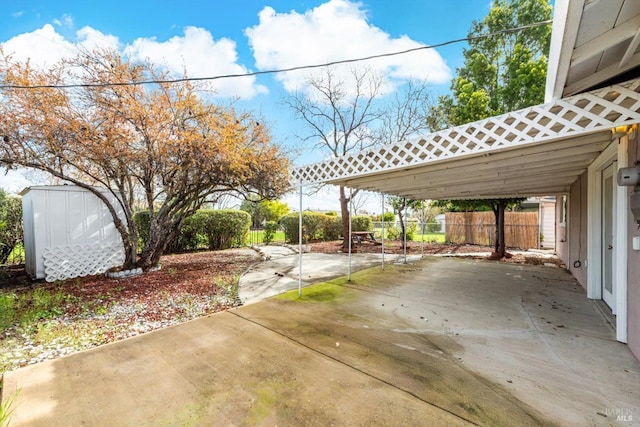 view of patio with an outbuilding, fence, driveway, a carport, and a storage shed